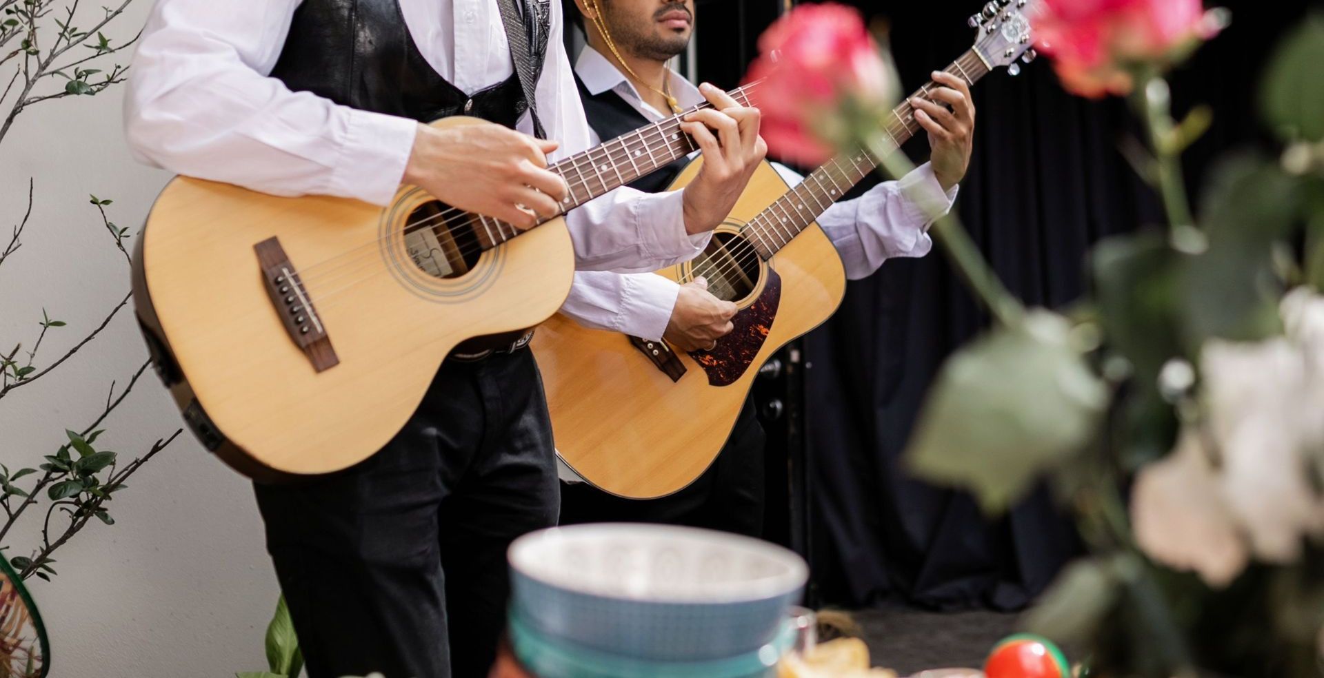 Two musicians in sombreros play guitars at a festive indoor event with food on the table.